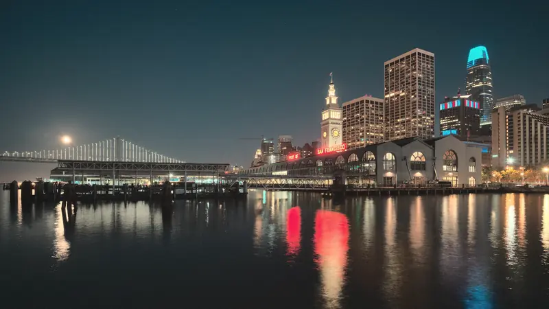 Photo of the Ferry Building and downtown towers reflected in the bay at night