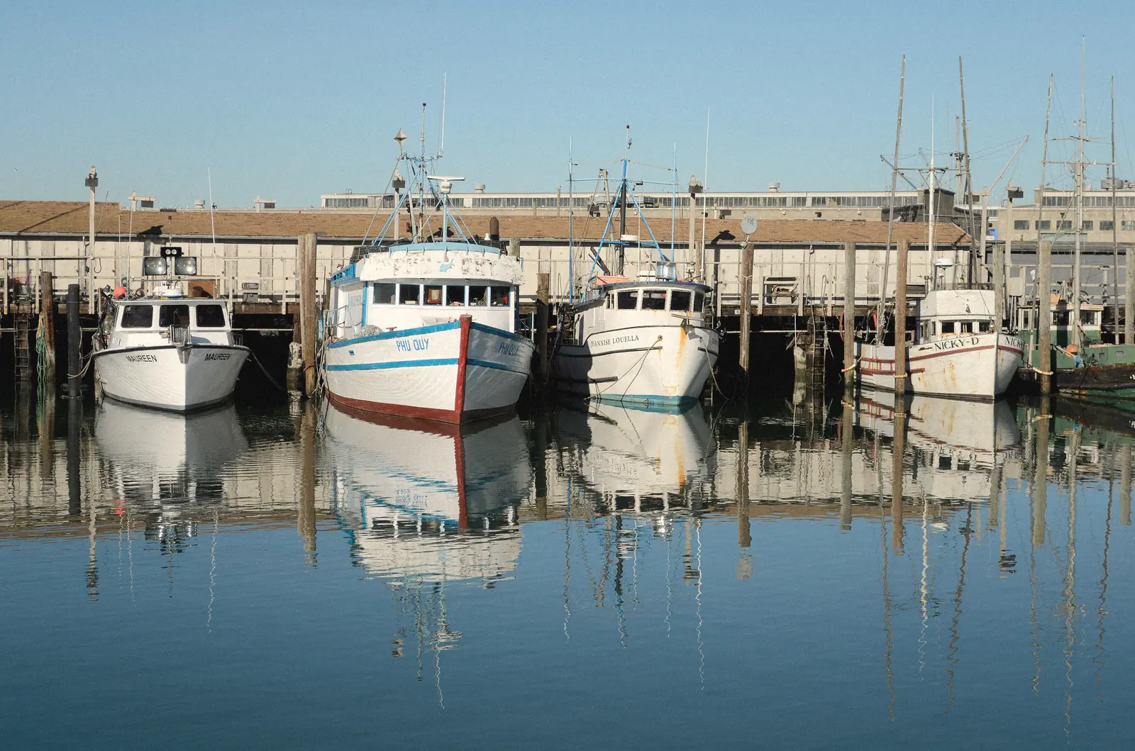 Photo of white fishing boats moored at Fisherman’s Wharf on a still morning